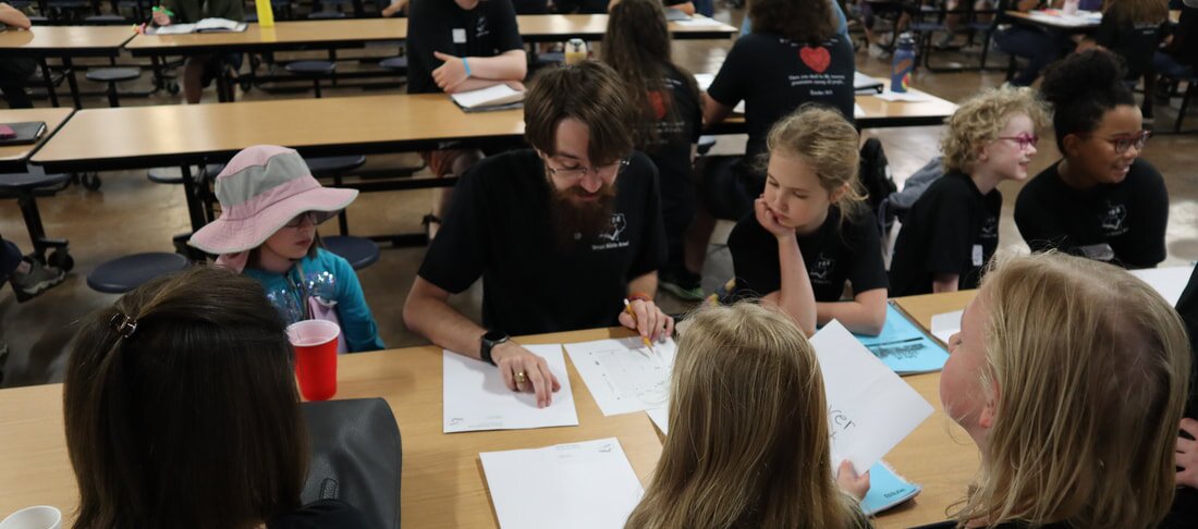 A coach studying pages around a table with elementary students during tribe time