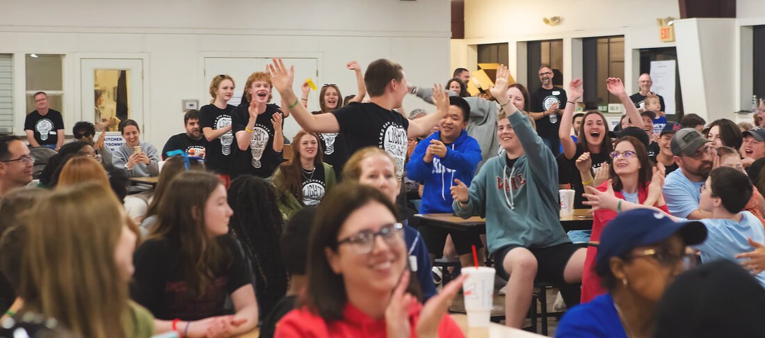 A room full of participants laughing and raising their hands during a group activity