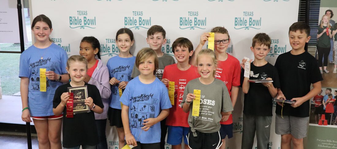 Elementary students smiling with their ribbons in front of the Texas Bible Bowl backdrop